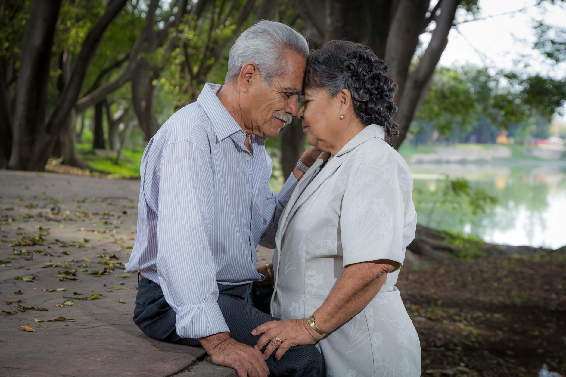 Starsza para przytulona na ławce w parku, cieszy się bliskością