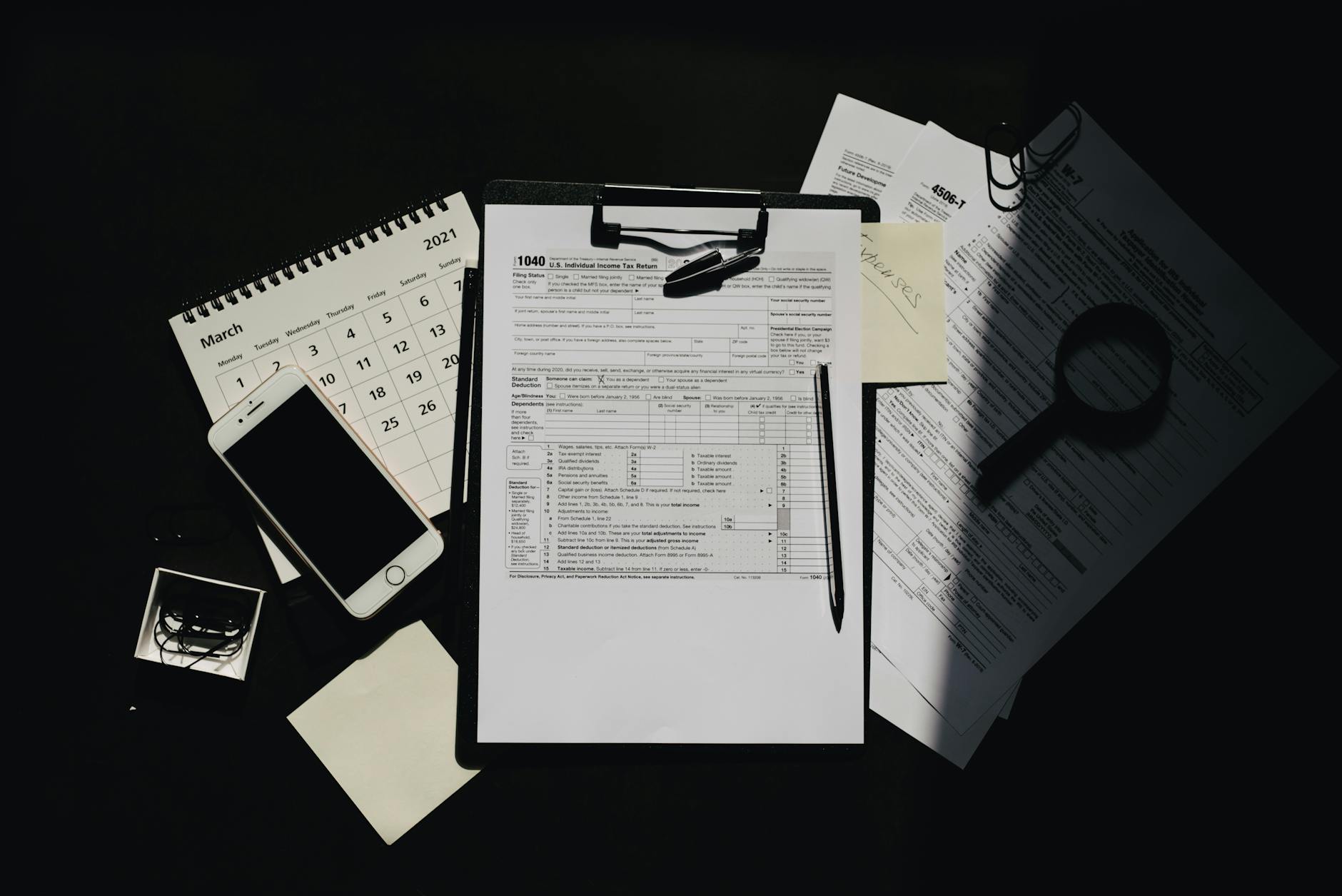 Dokumenty podatkowe, kalendarz i smartfon ułożone na ciemnym biurku